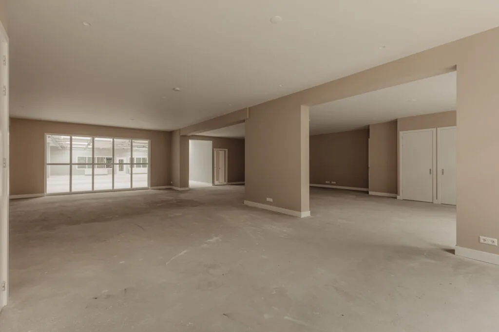 Ruime, lege binnenruimte aan de Henri Polaklaan met beige muren en grote ramen naar een atrium.